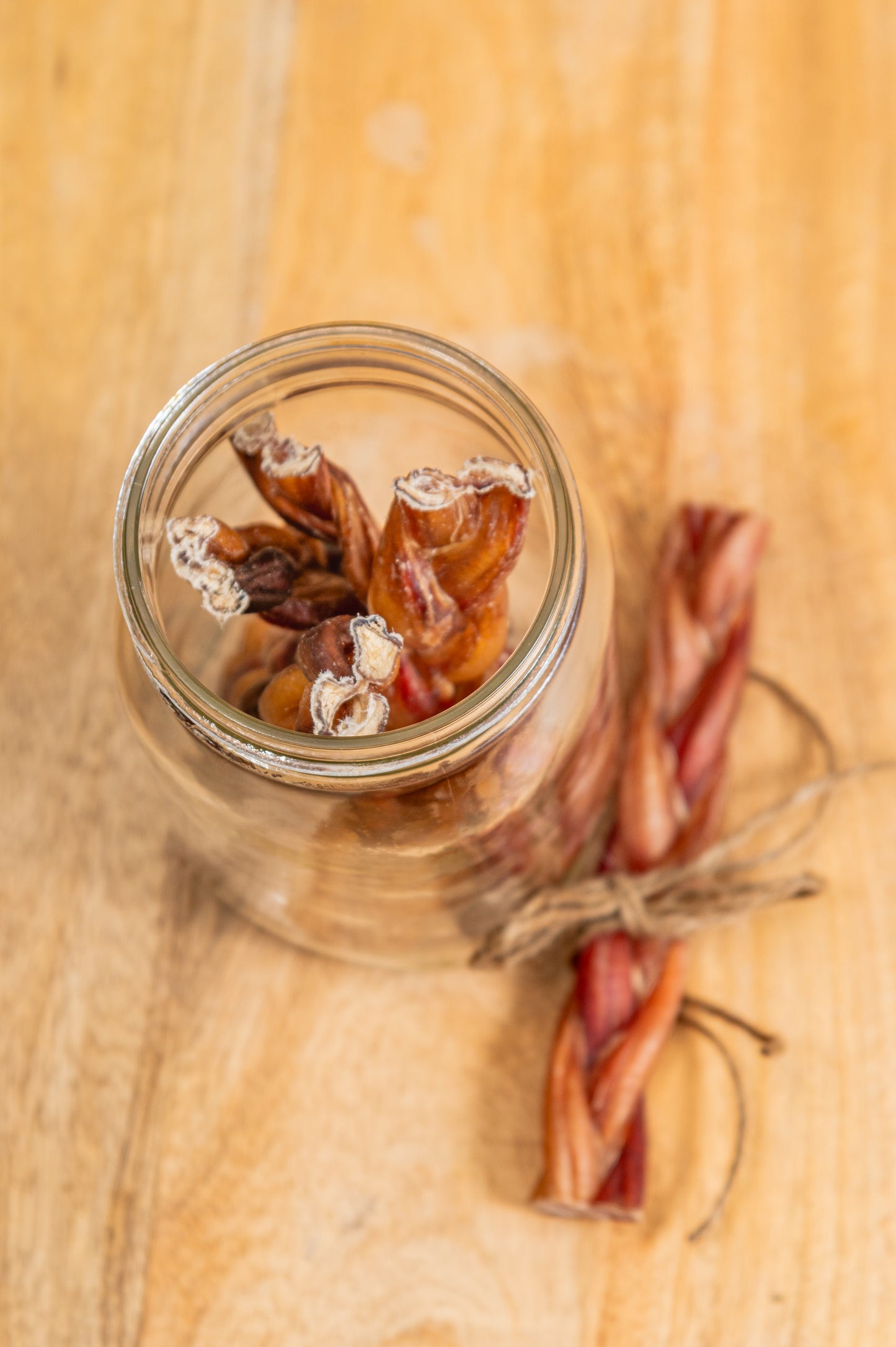 Braided bully sticks stored in a clear glass jar with twine, displayed on wood for rustic product styling
