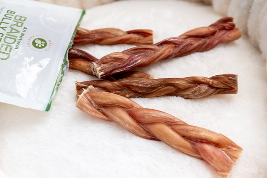 A close-up of Melico Pawtry’s all-natural braided bully sticks displayed on a soft white surface, partially shown with the product’s packaging in the corner.