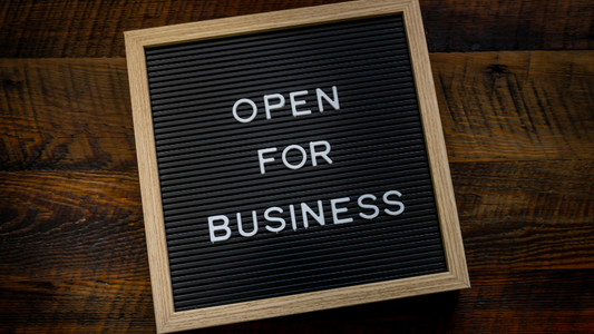 Letter board sign with the words “OPEN FOR BUSINESS” displayed on a dark wooden surface.