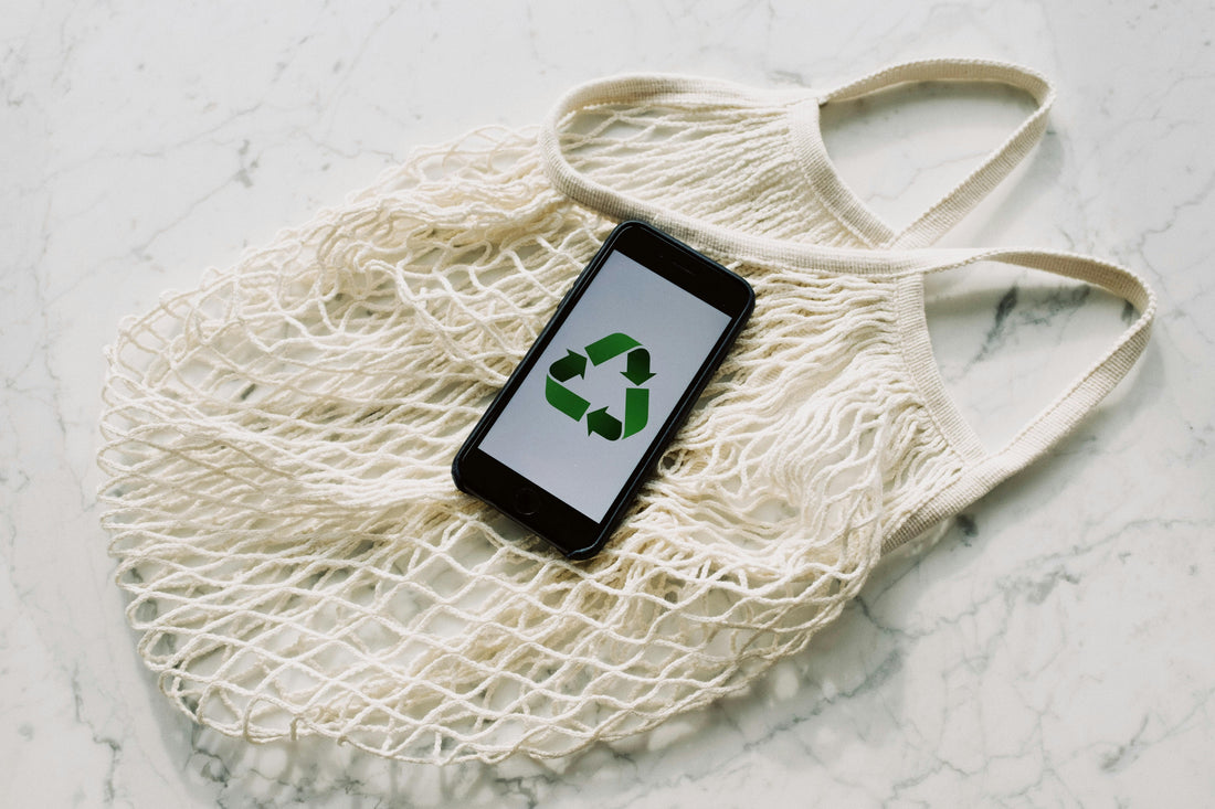 A smartphone displaying a green recycling symbol placed on top of a reusable cotton mesh bag, symbolizing sustainability and eco-friendly living.