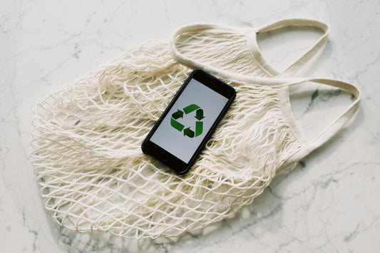 A smartphone displaying a green recycling symbol placed on top of a reusable cotton mesh bag, symbolizing sustainability and eco-friendly living.