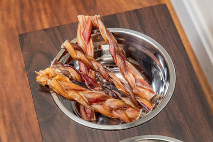 Braided beef bully sticks served in stainless steel dog bowl, natural dental chew for dogs in stylish pet feeder
